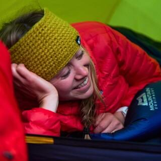 Mädchen liegt im Schlafsack im Zelt und lacht. Foto: Mountain Equipment 