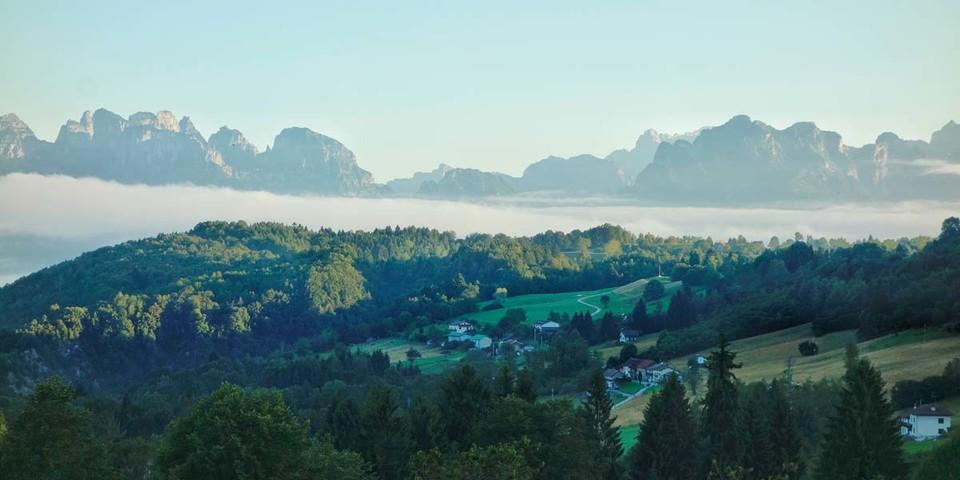 Bewaldete Hügel und kleine Ortschaften in den Belluneser Voralpen, dahinter die Schiara-Dolomiten. Foto: Joachim Chwaszcza
